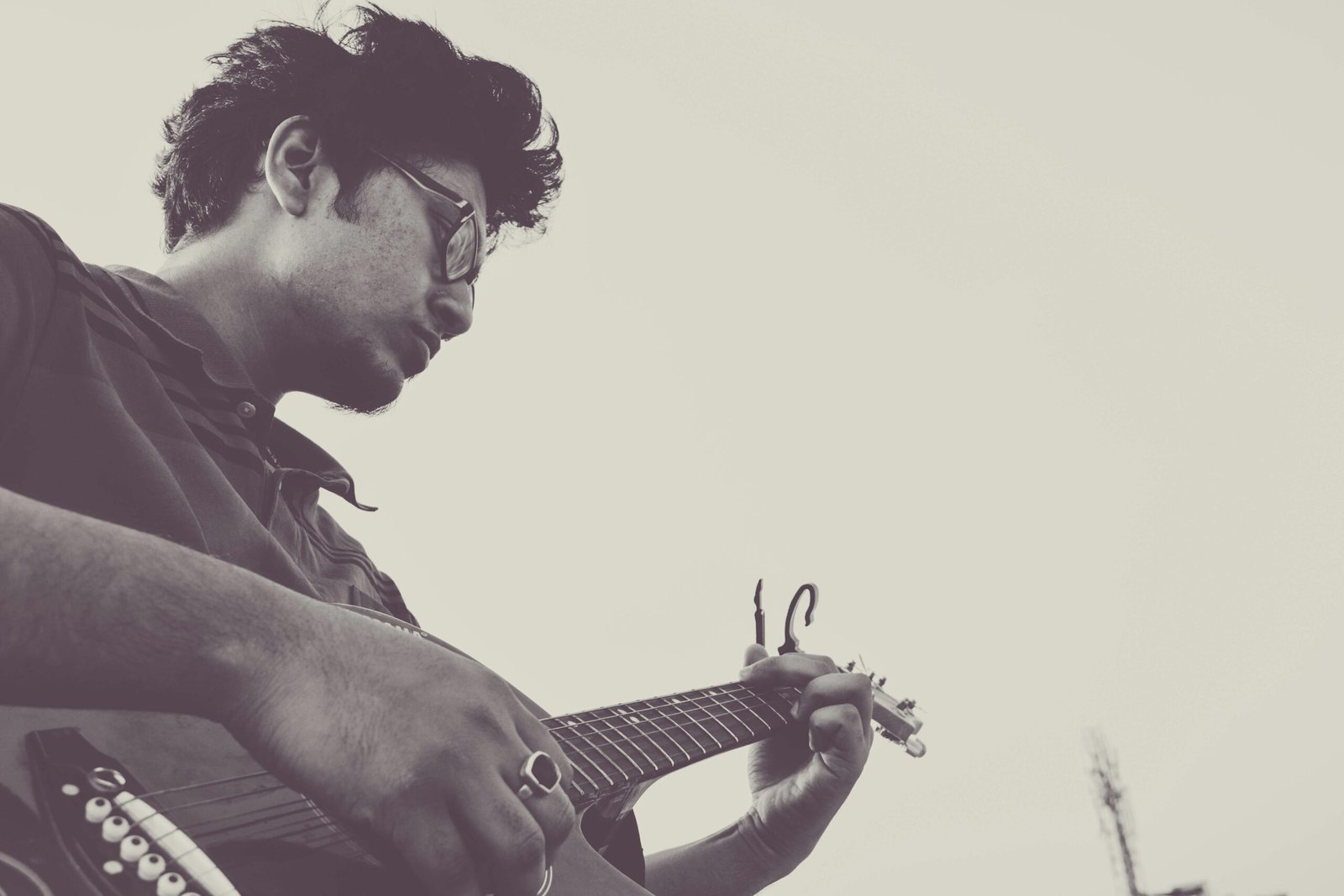 A black and white side view portrait of a male guitarist playing solo outdoors.